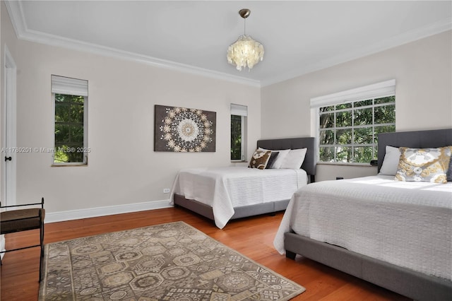 bedroom with an inviting chandelier, baseboards, ornamental molding, and wood finished floors