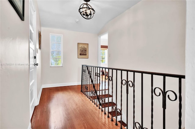 hallway with wood finished floors, baseboards, vaulted ceiling, a notable chandelier, and an upstairs landing