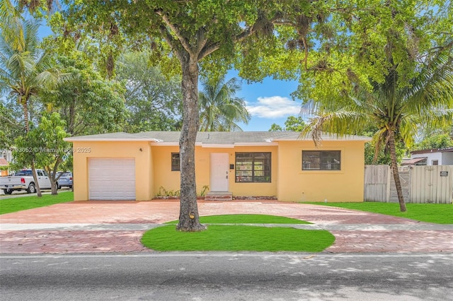 view of front of property with fence, a front yard, curved driveway, stucco siding, and an attached garage