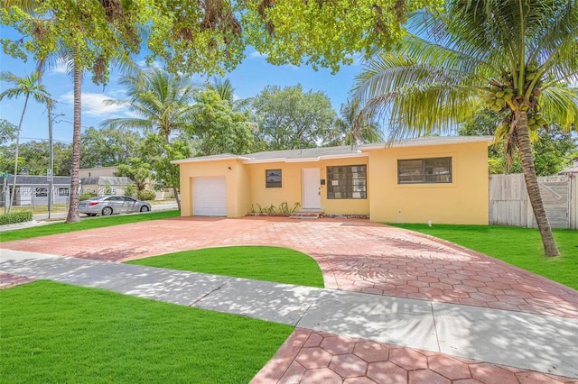 view of front of house with a front yard, decorative driveway, fence, an attached garage, and stucco siding