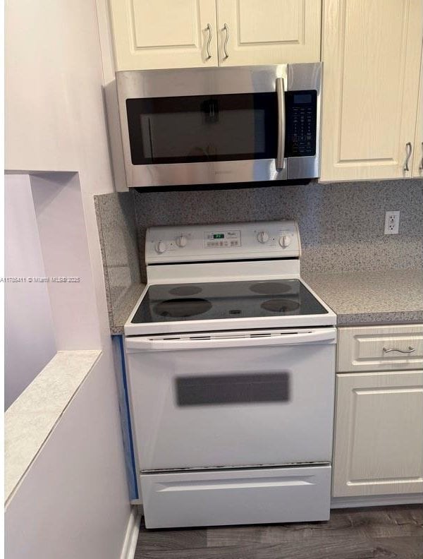 kitchen with white range with electric cooktop, light countertops, white cabinets, stainless steel microwave, and dark wood-type flooring
