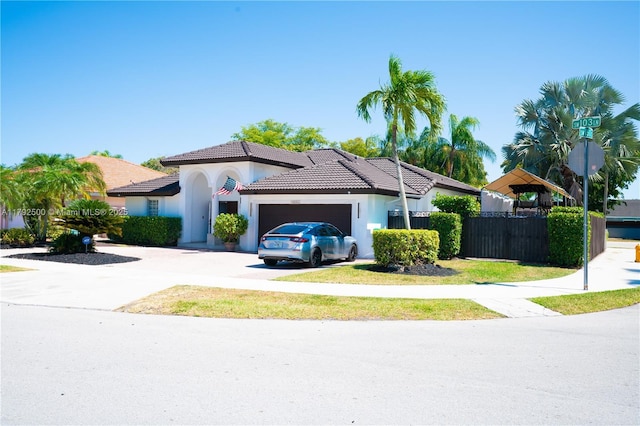 view of front facade featuring fence, stucco siding, a tiled roof, concrete driveway, and an attached garage