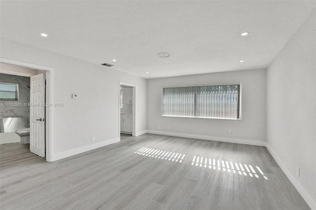 unfurnished bedroom with recessed lighting, baseboards, wood finished floors, and ensuite bath