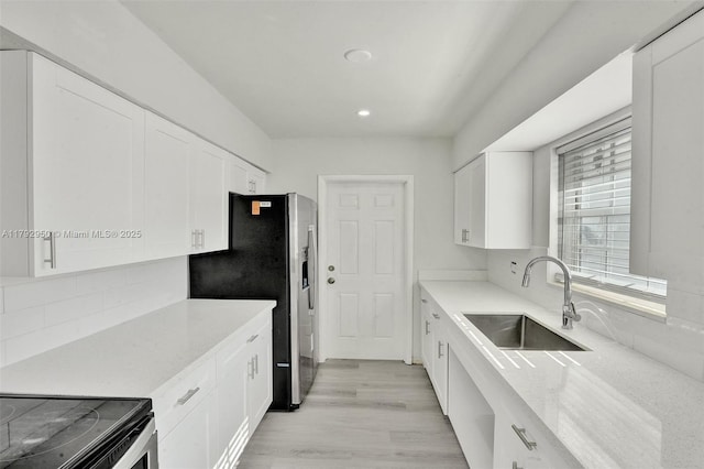 kitchen with white cabinets, stainless steel fridge, a sink, recessed lighting, and backsplash