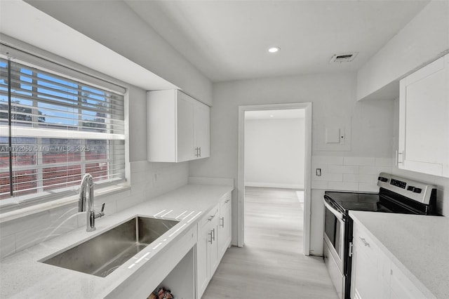 kitchen featuring visible vents, a sink, stainless steel electric range, and white cabinets