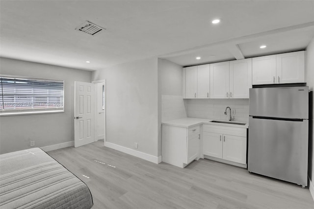 kitchen with a sink, light wood-style flooring, freestanding refrigerator, decorative backsplash, and visible vents