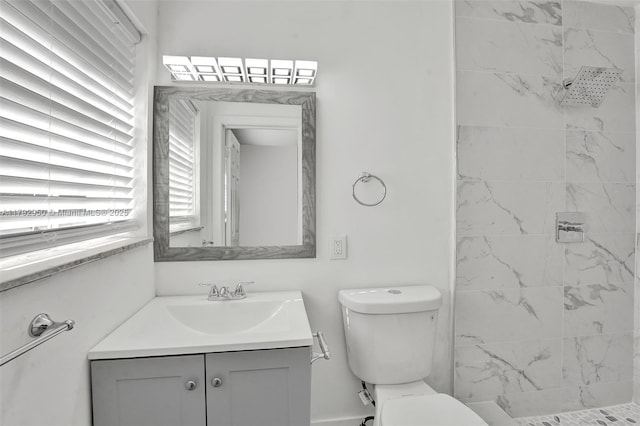 bathroom with toilet, tiled shower, and vanity