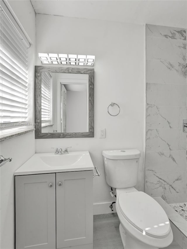 bathroom with toilet, a stall shower, baseboards, and vanity