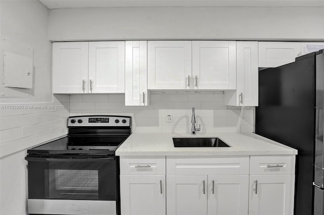kitchen featuring backsplash, stainless steel electric range, a sink, freestanding refrigerator, and white cabinetry
