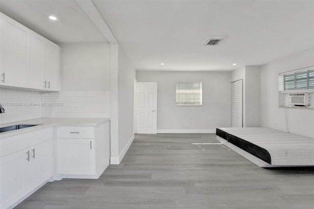 kitchen with decorative backsplash, light countertops, white cabinetry, cooling unit, and a sink