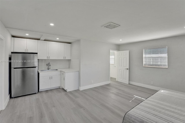 kitchen with freestanding refrigerator, recessed lighting, light wood-type flooring, white cabinetry, and a sink