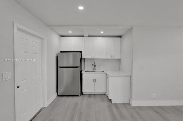 kitchen with white cabinets, a sink, light wood-style floors, freestanding refrigerator, and decorative backsplash
