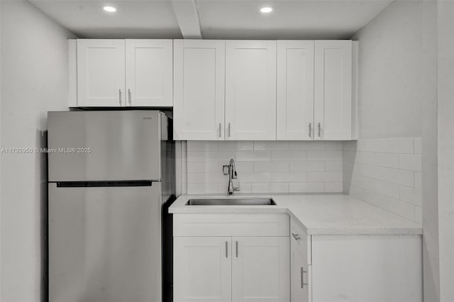 kitchen featuring backsplash, a sink, light countertops, white cabinets, and freestanding refrigerator