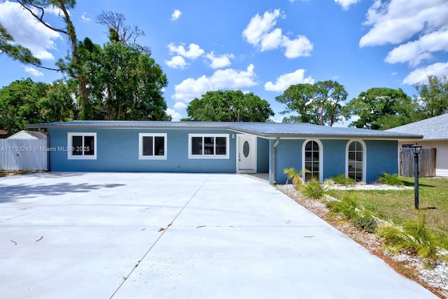 ranch-style house with fence, stucco siding, concrete driveway, and metal roof