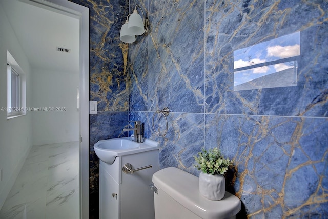 half bathroom featuring visible vents, tile walls, vanity, toilet, and marble finish floor