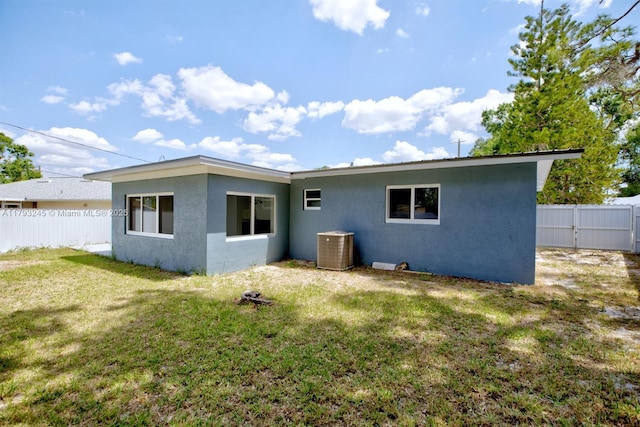 rear view of property featuring central AC, stucco siding, a yard, and fence