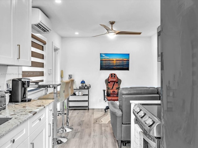 interior space with ceiling fan, a wall unit AC, light stone counters, light wood-style floors, and white cabinetry