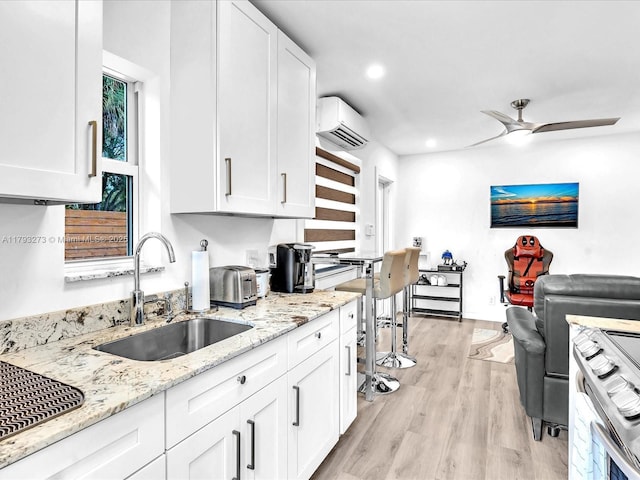 kitchen featuring a sink, a wall mounted AC, light wood finished floors, and white cabinetry