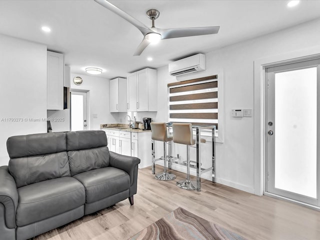 living room with light wood-style floors, a wall mounted air conditioner, baseboards, recessed lighting, and a ceiling fan