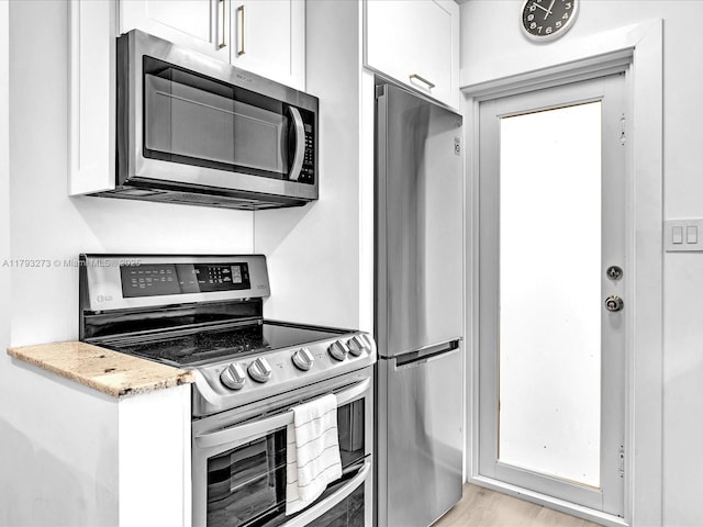 kitchen with white cabinets, light stone countertops, appliances with stainless steel finishes, and light wood-style flooring