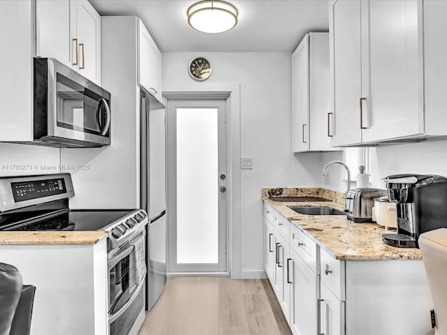 kitchen with a sink, light stone counters, white cabinets, light wood finished floors, and stainless steel appliances