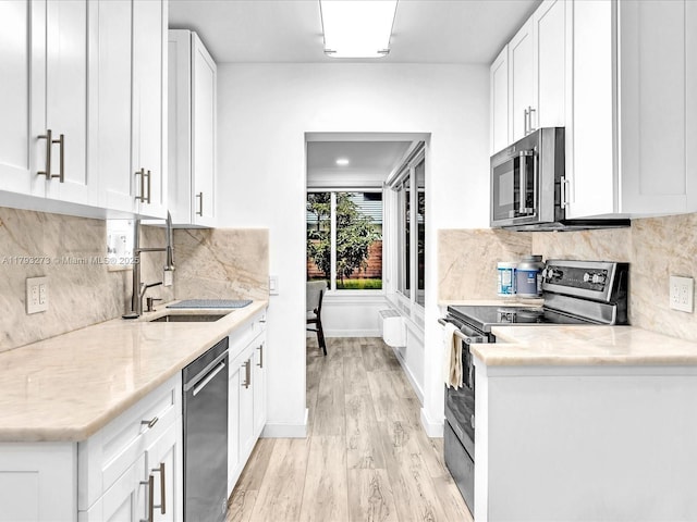 kitchen featuring backsplash, appliances with stainless steel finishes, a sink, light wood finished floors, and white cabinetry