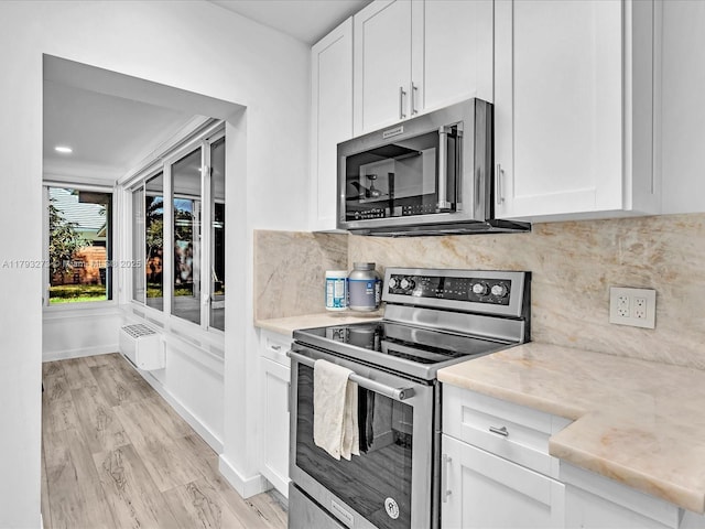 kitchen with appliances with stainless steel finishes, tasteful backsplash, light wood-type flooring, and white cabinetry