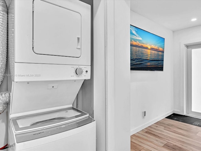 clothes washing area featuring stacked washer / drying machine, laundry area, recessed lighting, baseboards, and wood finished floors