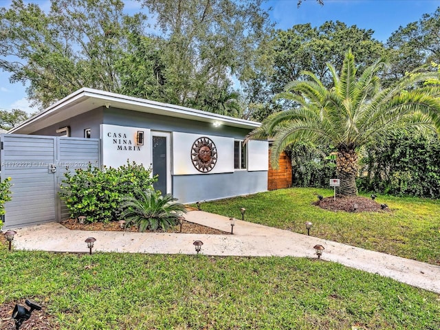 view of front of house featuring stucco siding, a gate, and a front lawn