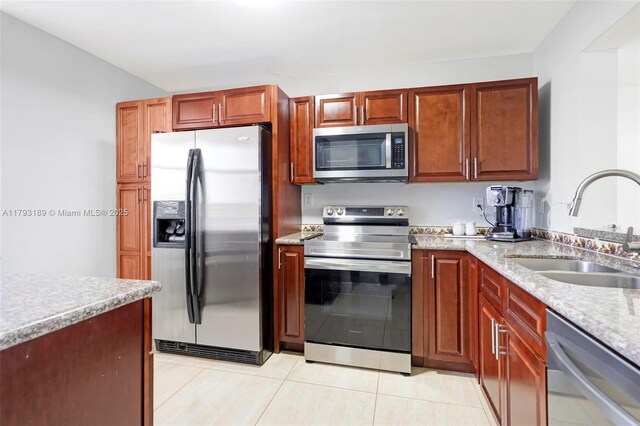 kitchen featuring a sink, appliances with stainless steel finishes, light tile patterned floors, and light stone countertops
