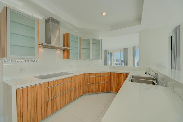 kitchen with modern cabinets, light countertops, black electric cooktop, wall chimney exhaust hood, and a sink