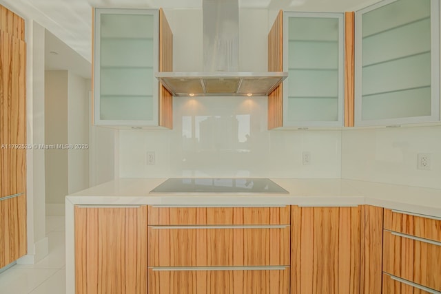 kitchen with light countertops, black electric cooktop, wall chimney exhaust hood, backsplash, and modern cabinets