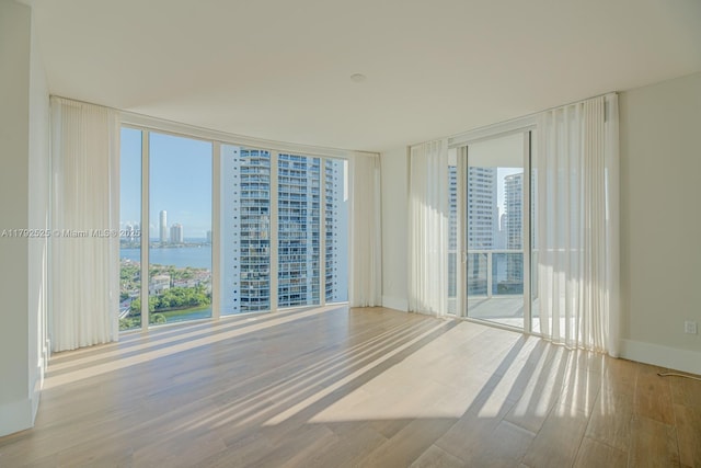 unfurnished room featuring a view of city, wood finished floors, baseboards, a water view, and expansive windows