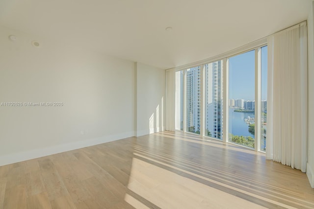 unfurnished room featuring a view of city, a water view, wood finished floors, and a wall of windows