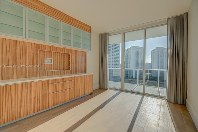 unfurnished room featuring a view of city, baseboards, expansive windows, and wood finished floors