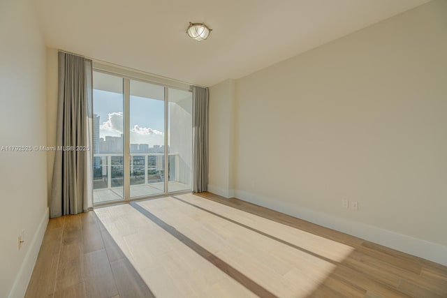 unfurnished room featuring expansive windows, baseboards, and wood finished floors