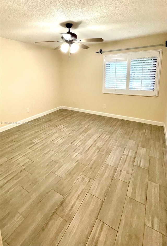 empty room featuring baseboards, a ceiling fan, a textured ceiling, and wood finished floors