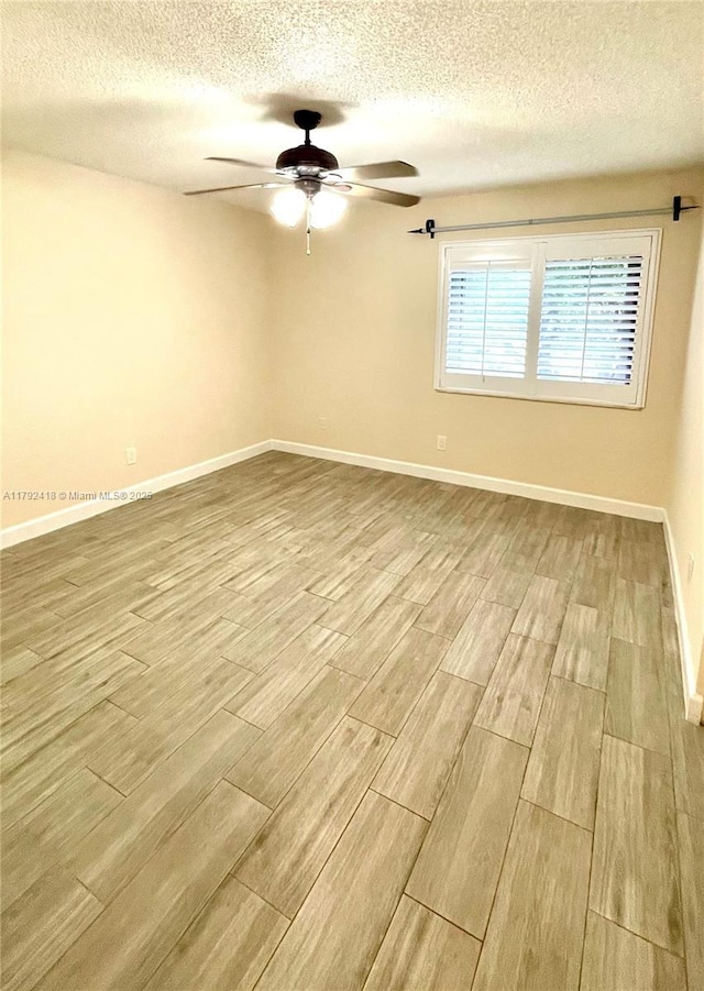 spare room with baseboards, a ceiling fan, a textured ceiling, and wood finished floors