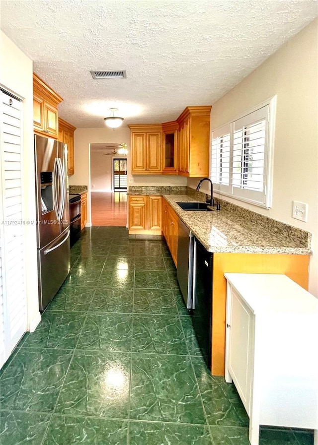 kitchen with visible vents, brown cabinets, stainless steel fridge with ice dispenser, light stone counters, and a sink