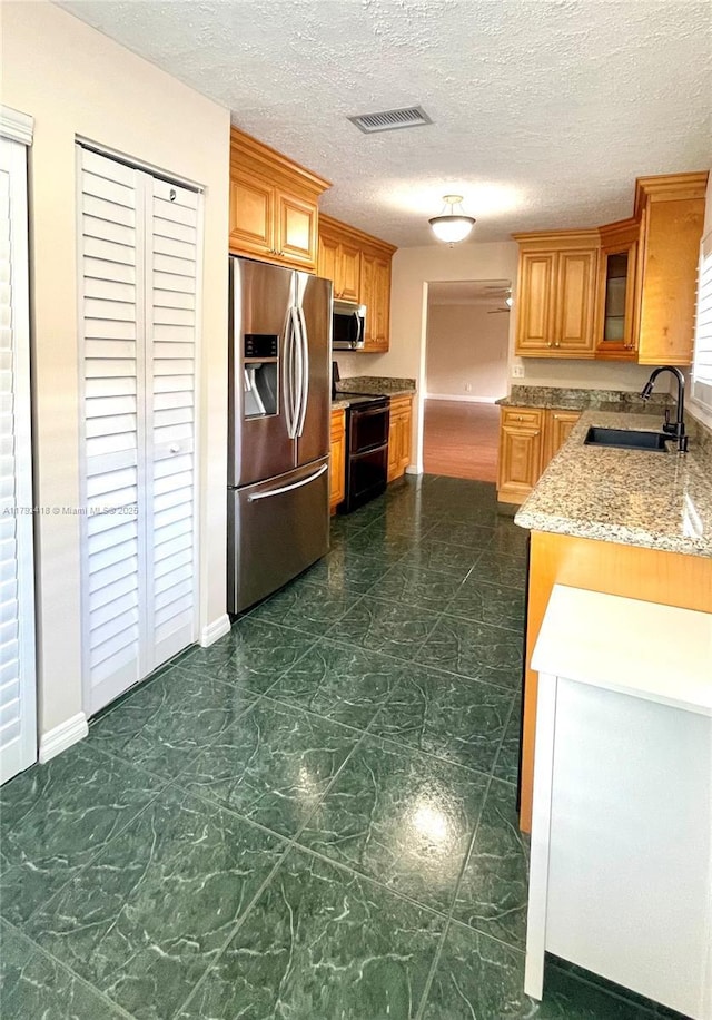 kitchen with visible vents, baseboards, light stone counters, a sink, and stainless steel appliances