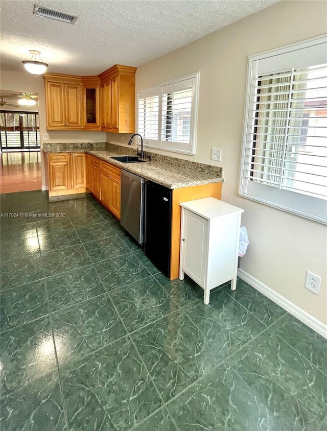 kitchen with a sink, a textured ceiling, brown cabinetry, stainless steel dishwasher, and visible vents