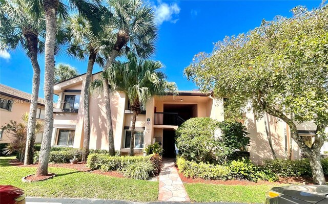 view of front of home with a balcony, a front lawn, and stucco siding