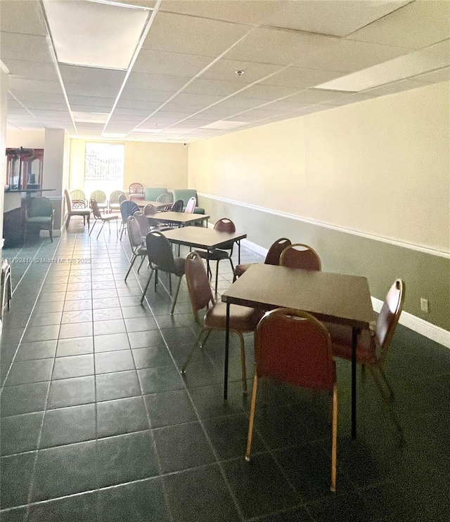 dining space featuring dark tile patterned flooring, baseboards, and a drop ceiling