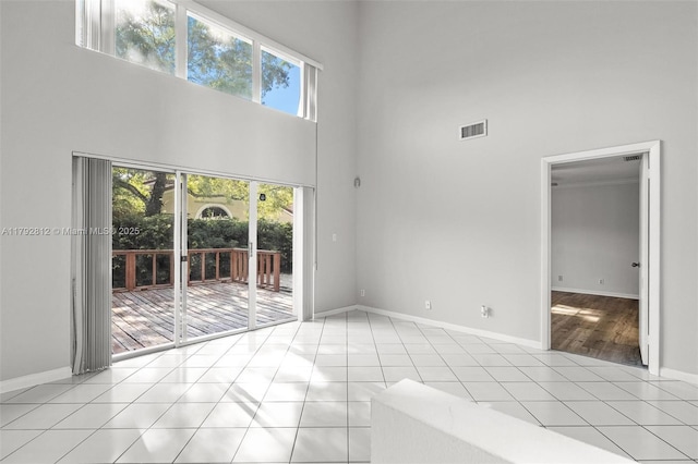 empty room with a healthy amount of sunlight, light tile patterned floors, a high ceiling, and visible vents