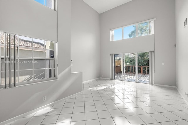 tiled spare room featuring baseboards, a towering ceiling, and visible vents
