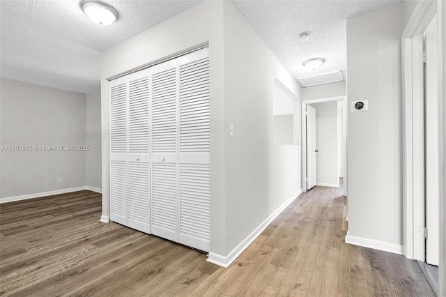hall featuring baseboards, a textured ceiling, light wood-style flooring, and attic access