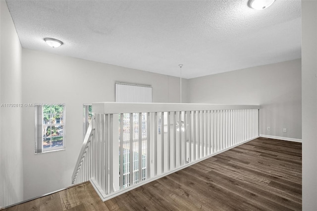 corridor with baseboards, a textured ceiling, and wood finished floors