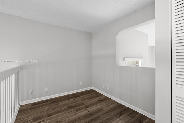 unfurnished room featuring baseboards, a textured ceiling, and dark wood-style flooring