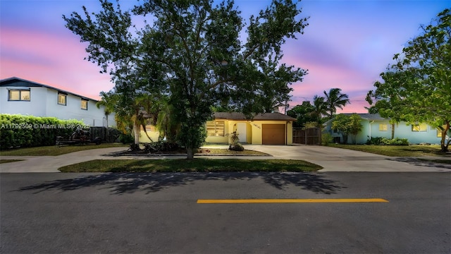 view of property hidden behind natural elements with fence, driveway, and a garage