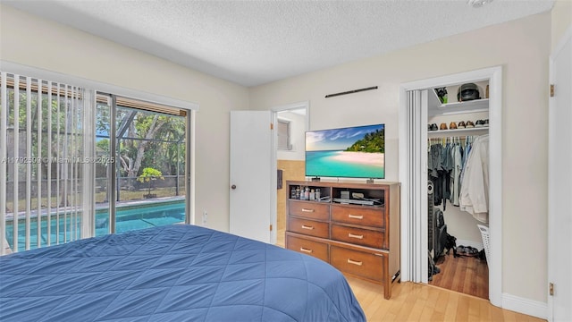 bedroom with access to outside, a walk in closet, light wood-style floors, a textured ceiling, and a closet